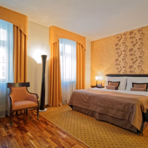 Double Rooms Double bedroom at Skaritz Hotel Bratislava with king bed, ornate orange wallpaper, floor lamp, and armchair.