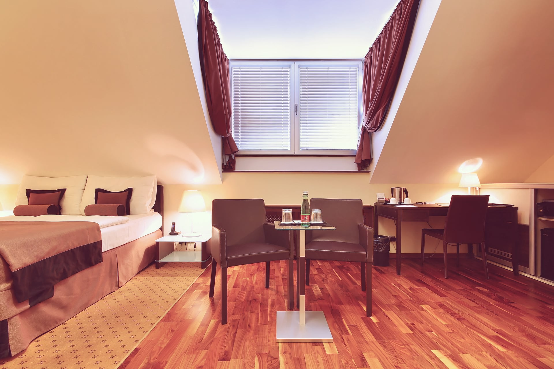 Attic hotel room featuring two brown leather armchairs, work desk, and dormer window at Skaritz Hotel.
