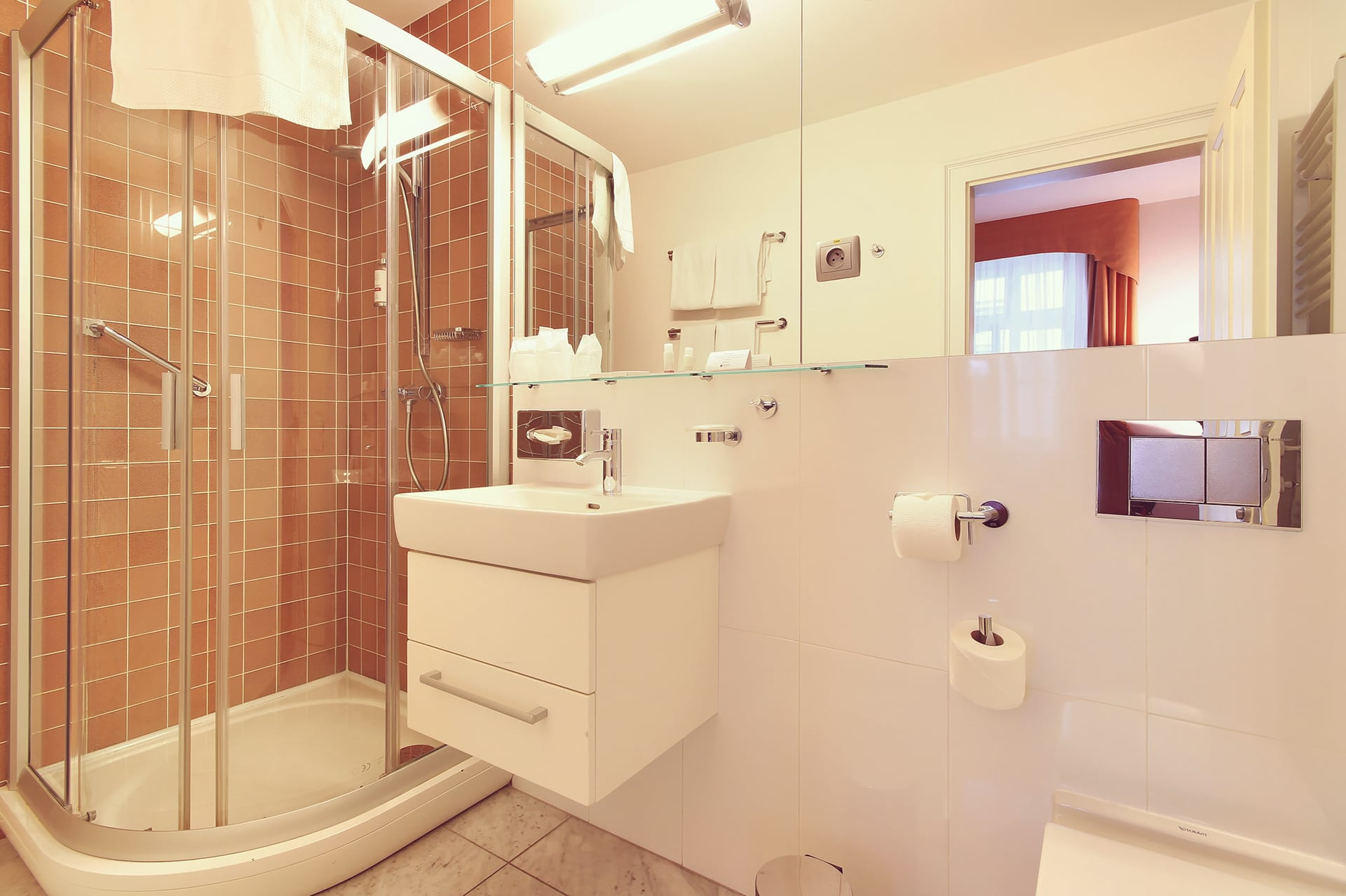 Hotel bathroom featuring glass shower cabin, white floating sink, mirror, and toilet.
