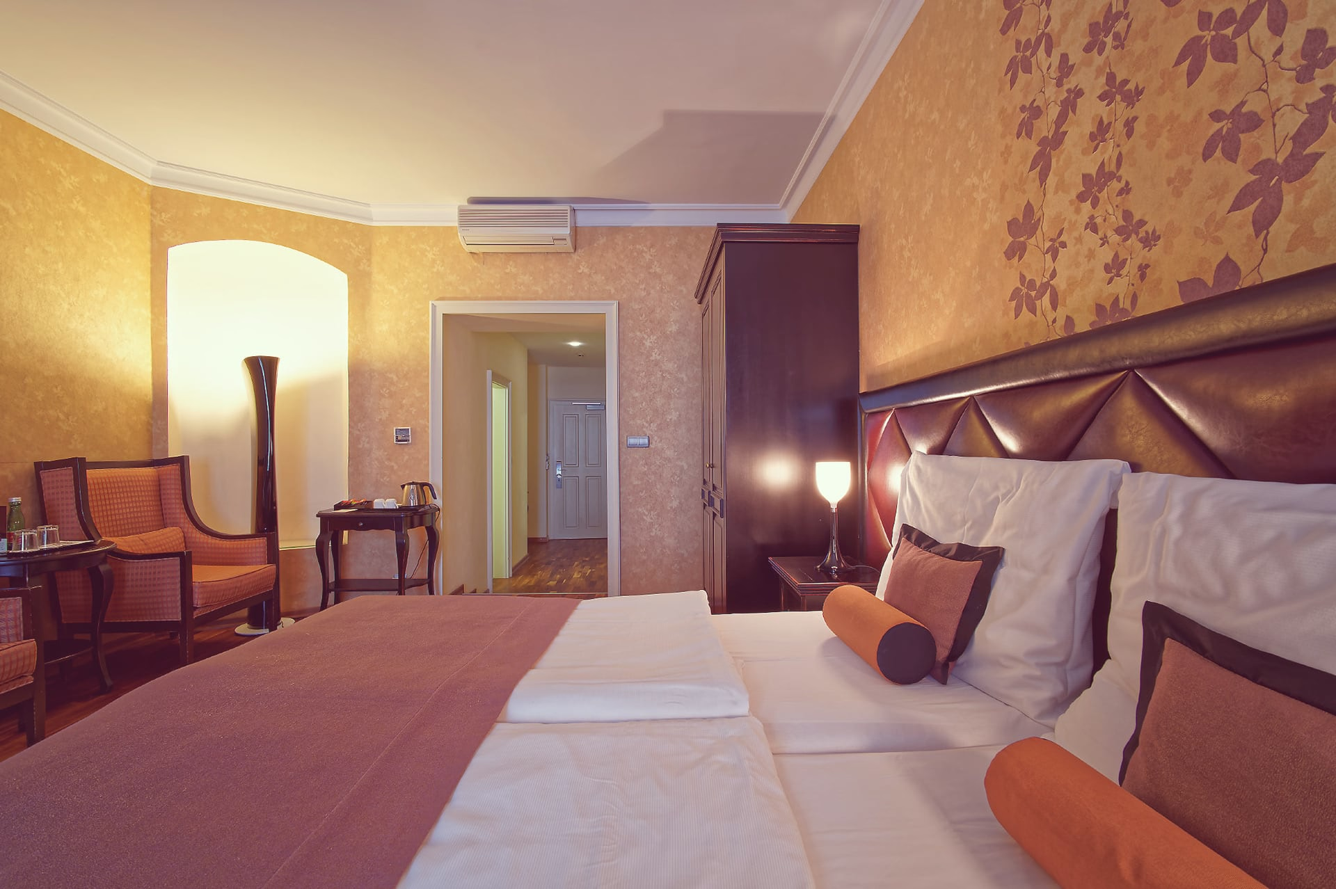 Angle shot of double bed looking toward room entrance hallway and seating corner.