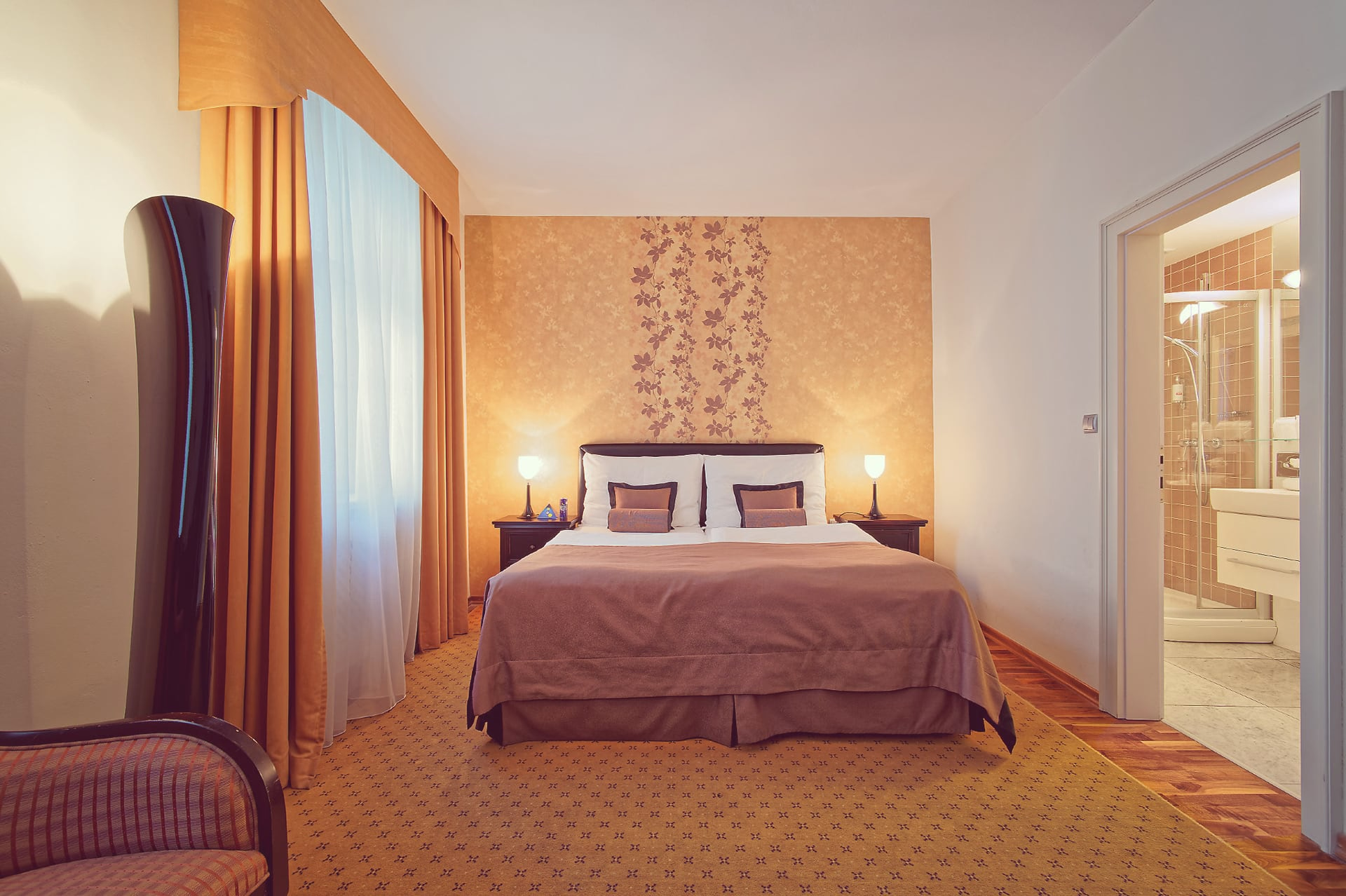 Frontal view of a king bed with patterned accent wallpaper and an en-suite bathroom at Skaritz Hotel Bratislava.