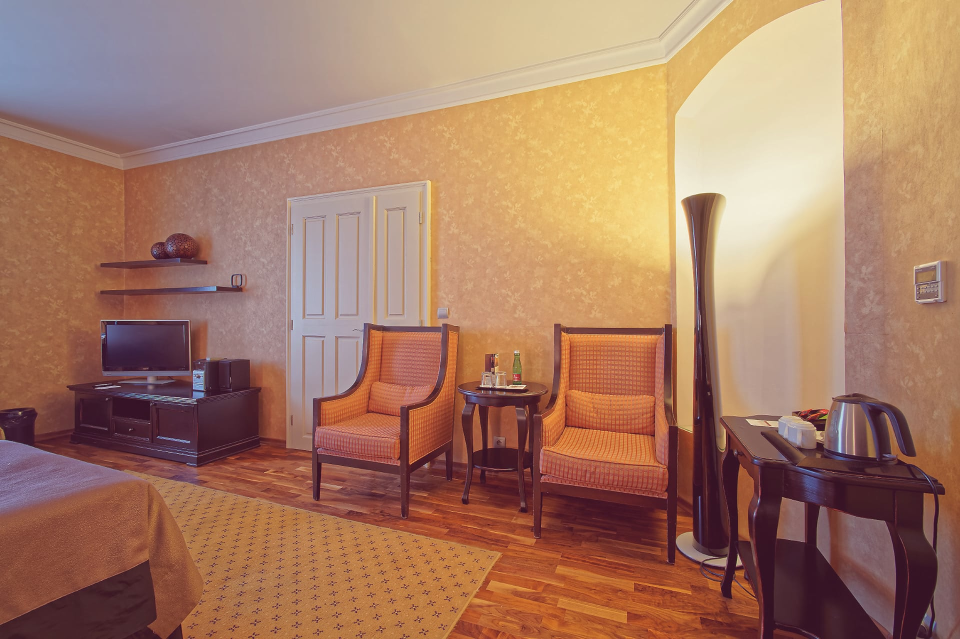 Hotel room lounge area with two patterned armchairs, small drinks table, and TV console at Skaritz Hotel.