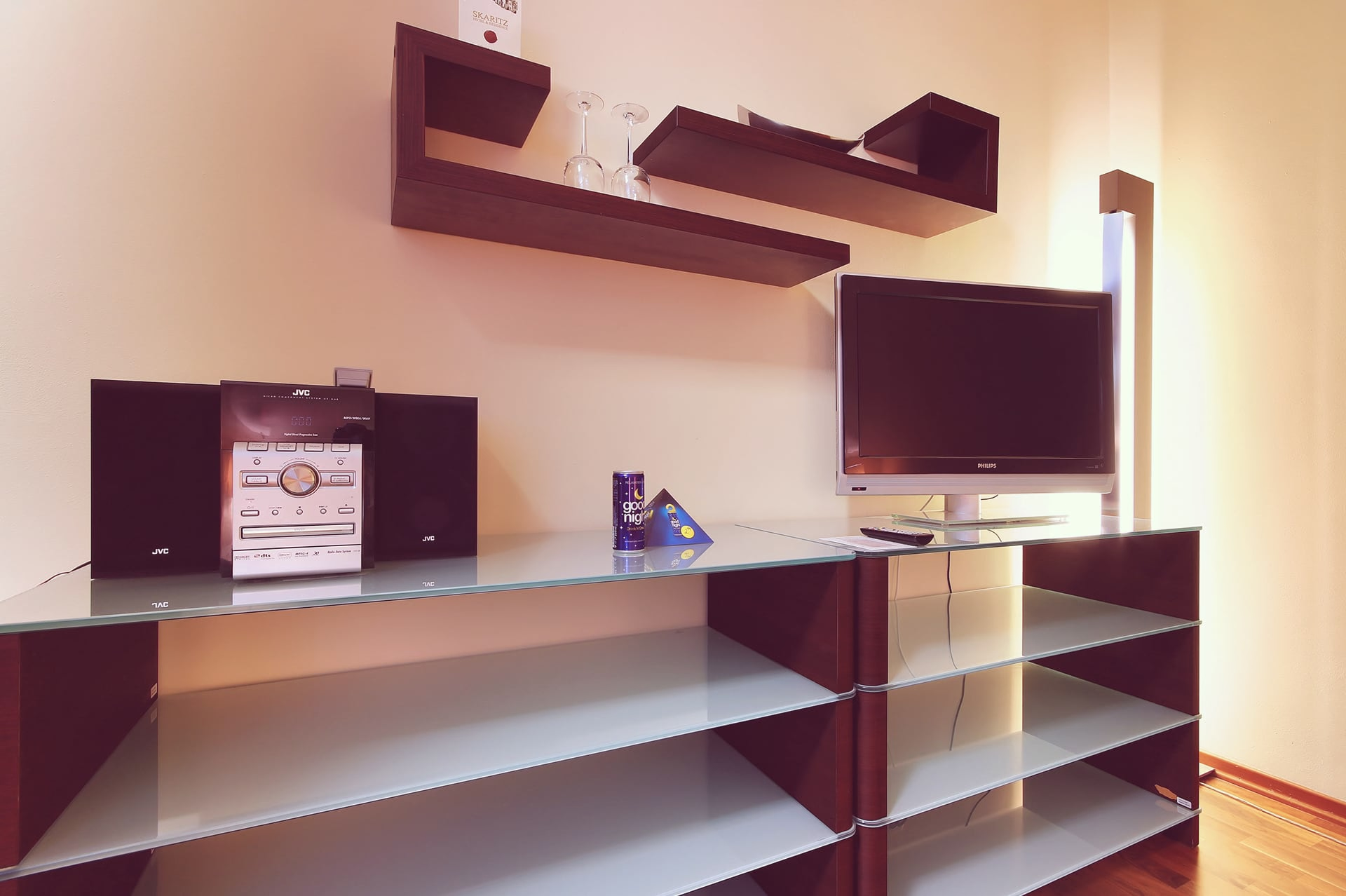 Media console with flat-screen TV, JVC audio system, glass shelves, and wall-mounted shelving.