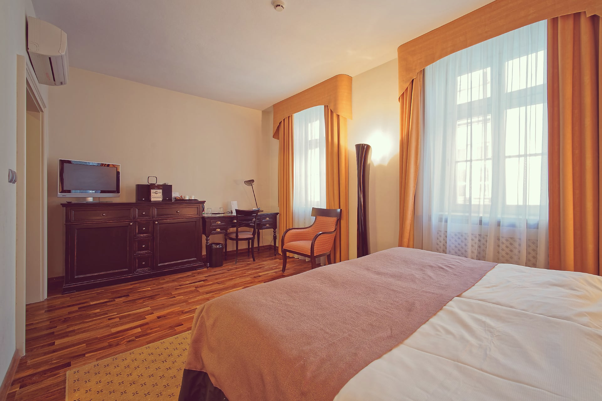 Spacious double room featuring dark wood TV dresser, writing desk, and large windows.