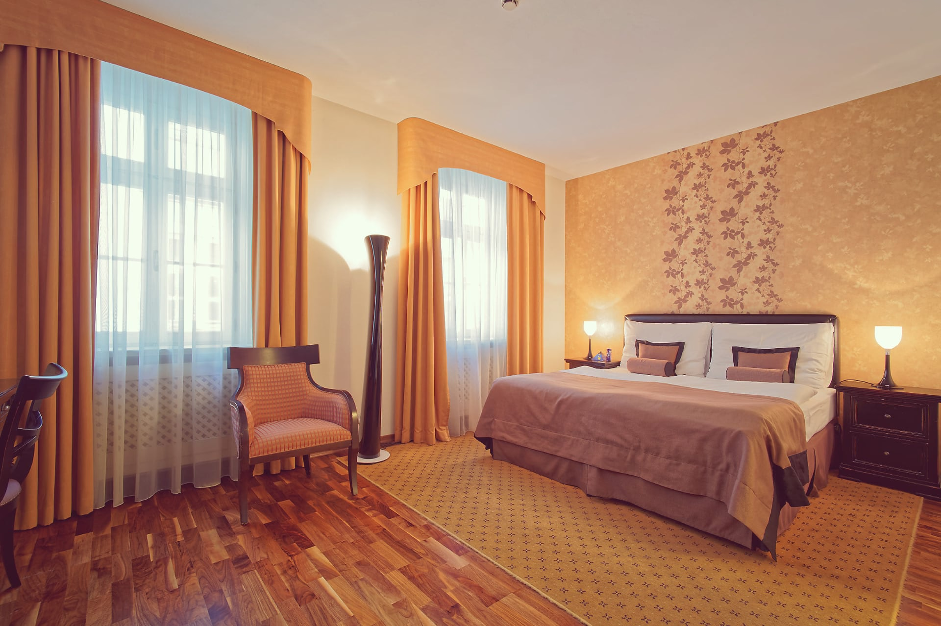 Wide view of hotel room layout showing king bed, wooden flooring, and tall window curtains at Skaritz Hotel.