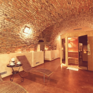 Hotel wellness area under historic brick vaulted ceilings featuring a wooden Finnish sauna cabin and wicker relaxation loungers with tea set.